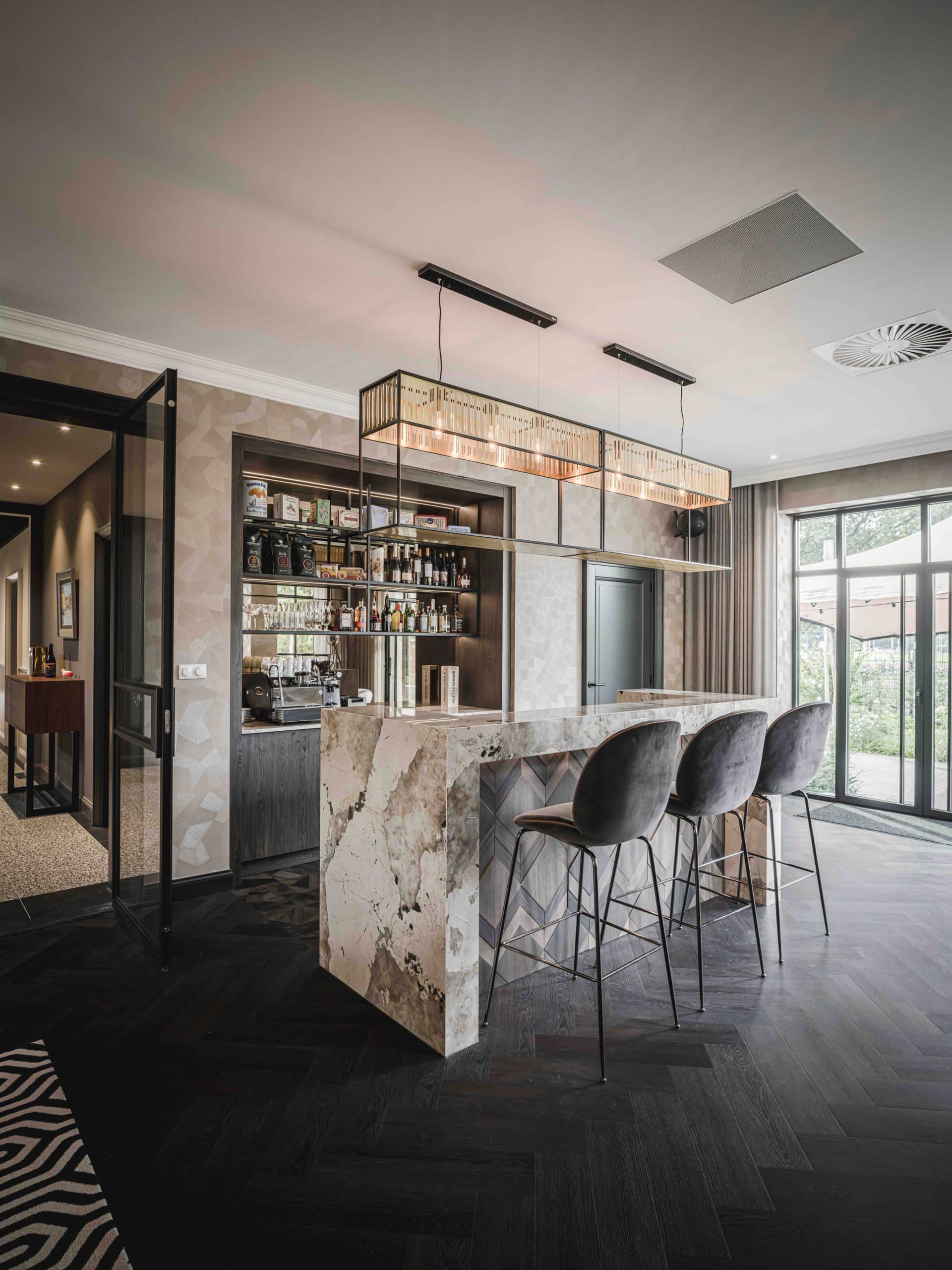 Bar en pierre naturelle Dekton Khalo avec un présentoir à bouteilles design en arrière plan dans une pièce sobre et contrastée